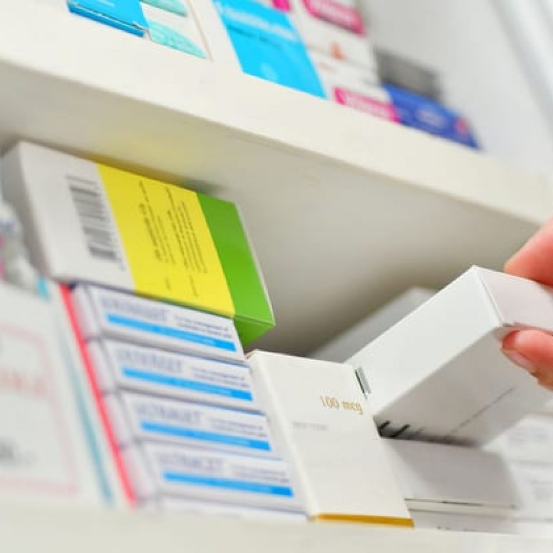 Hand nimmt Medikament aus Regal in Apotheke.